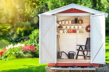 Garden shed filled with gardening tools with green sunny garden in the background.