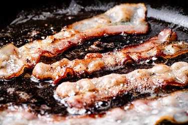 Pieces of bacon are fried in boiling oil with air bubbles