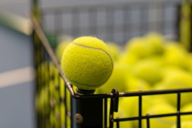 yellow tennis ball close-up on the edge of a black cart with tennis balls on a tennis court with a blurred background