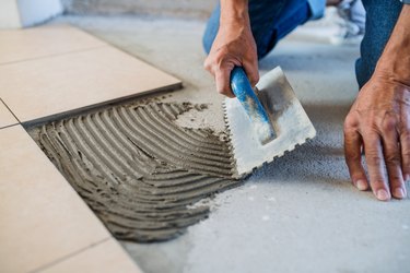 Midsection of senior man laying tile floor in new home.