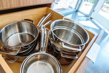 Wide Angle Close-Up Shot of Stainless Steel Pots and Pans in a Wooden Drawer in a Trendy Kitchen