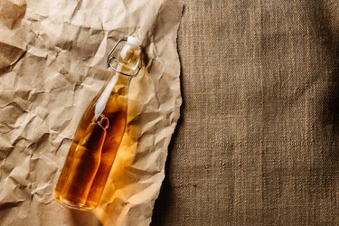 A bottle of apple cider or vinegar on a background of craft paper and burlap.