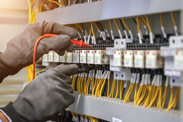 Electrical engineer using digital multi meter to check current voltage at circuit breaker in main distribution board.