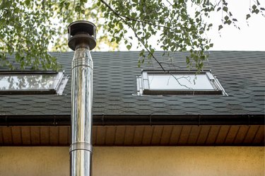 Stainless steel chimney flue on tile-covered roof with windows at country cottage