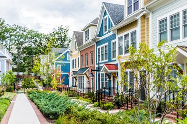 Row of colorful, red, yellow, blue, white, green painted residential townhouses, homes, houses with brick patio gardens in summer