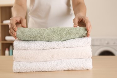 Woman with folded clean terry towels at table in laundry room, closeup