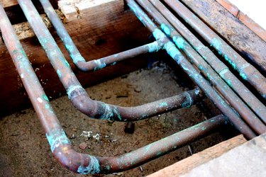 Closeup image of old copper pipes under floor.