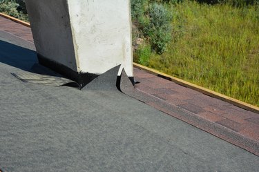 Asphalt roofing shingles installation and waterproofing chimney problem area.  Covering the roof with asphalt shingles on installed underlayment around chimney using a waterproofing flashing.