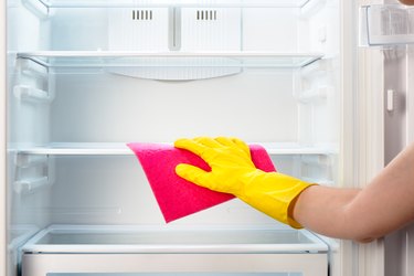 Woman's hand in yellow glove cleaning refrigerator with pink rag
