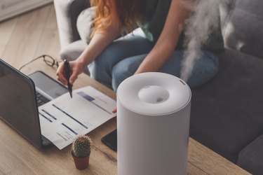Woman freelancer uses a household humidifier in the workplace at home office with a laptop and documents.
