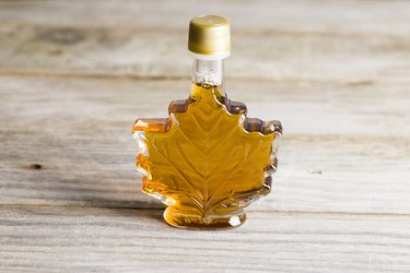 Maple syrup in glass bottle isolated on wooden background