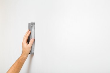 Young adult man hand polishing white wall with sanding sponge. Closeup. Empty place for text.