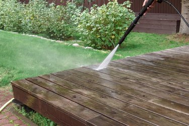 Cleaning a deck with high pressure power washer. Washing terrace wood planks and cladding walls.