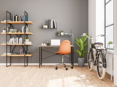 Scandinavian-style home office with bookshelves, desk/chair, houseplant, and bicycle by window.