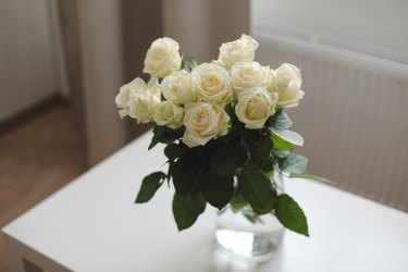 glass vase with white roses on white table indoors