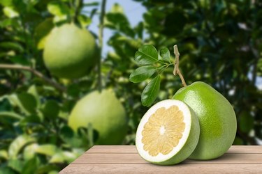 Pomelo fruit with green leaf and half sliced on wooden table with garden background.