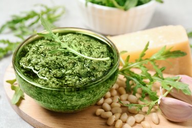 Bowl of tasty arugula pesto and ingredients on table