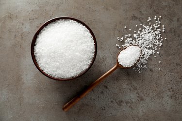 Bowl and spoon with natural sea salt on grey table, flat lay