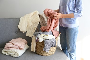 Bunch of sweaters of different material and knitting pattern in pile on gray sofa.
