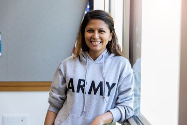 Female army vet leans against window and smiles for camera.