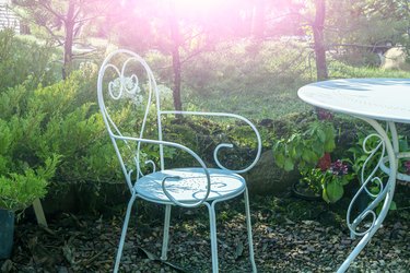 White metal iron chair and table outdoors. Retro styled furniture in magic green summer garden, symbols of Alice in Wonderland.