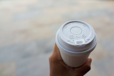 Man's hand holding a disposable coffee cup with a white polypropylene number 5 plastic lid