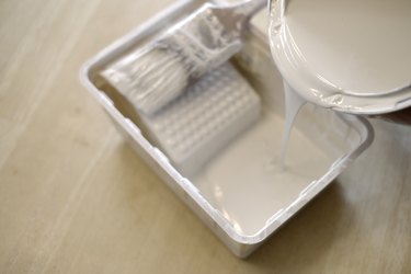 Pouring white paint into plastic paint bin with paintbrush for painting home