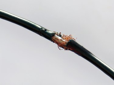 Damaged black electric cord on light background. Dangerous broken power electrical cable