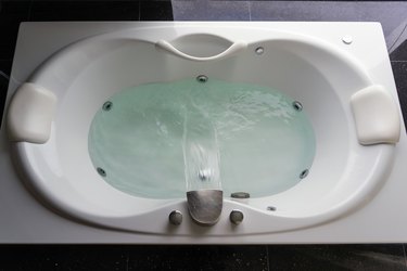 Empty white massaging jetted bathtub on black polished stone floor