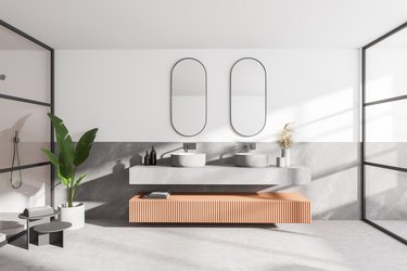 Interior of modern bathroom with white and wooden walls, concrete floor, double sink with two mirrors above it and shower cabin.