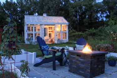 Beautiful garden with fire pit andirondack chairs and greenhouse