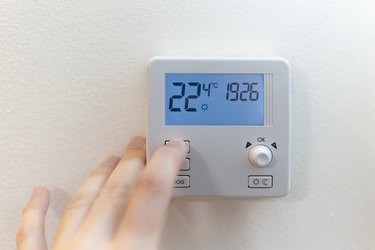 Close up view of a hand adjusting the heating temperature. Digital thermostat on the wall of the house