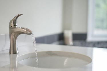 Close-Up Of Water Running From Faucet In Bathroom At Home