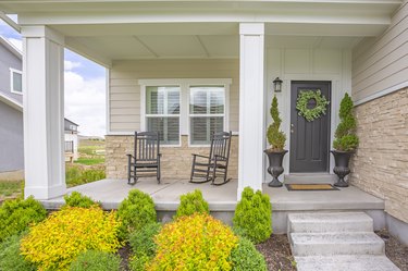 Home facade with stairs leading to porch with pillars and gray door with wreath