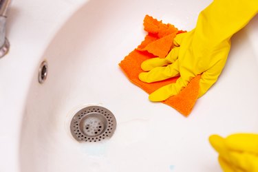 hand in a yellow rubber glove wipes the sink in the bathroom