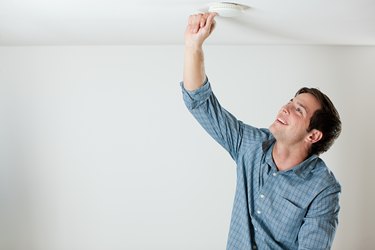 Young man testing smoke alarm on ceiling