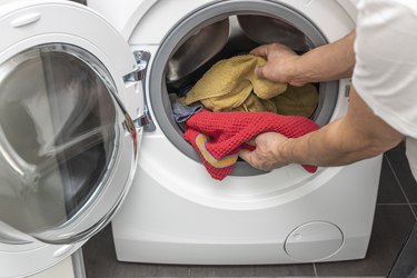 Close up view of man loading clothes to washing machine.