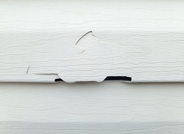 Vinyl siding missing pieces and cracked on the outside of a home.