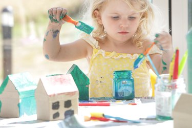 Child painting small cardboard houses.