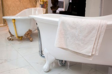 a white terry towel lies on a cast-iron bathtub on a ceramic tile floor in a store.