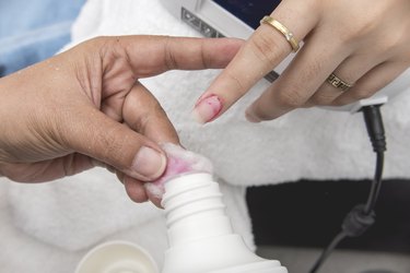 Manicurist using a cotton ball soaked in acetone. to remove leftover polish from customer's index fingernail.