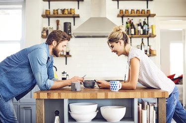 Smiling couple with digital tablets leaning on kitchen island