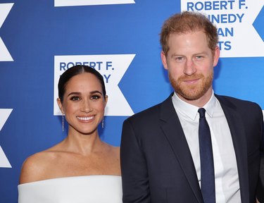 Prince Harry and Meghan Markle standing together in front of a blue backdrop.