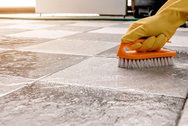 Hands wearing yellow rubber gloves are using a plastic floor scrubber to scrub the tile floor with a,Romania