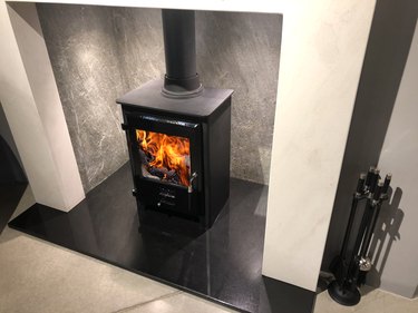 Image of square cast iron woodburner / contemporary log wood burning stove fireplace mantle with orange fire flames burning and generating heat to warm up room instead of gas boiler central heating, modern multifuel stove wood burner stand / chimney flue