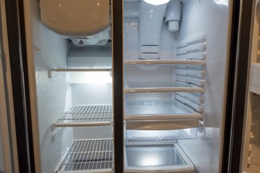 View of a white, empty fridge with the door wide open to see several shelves and drawers devoid of food