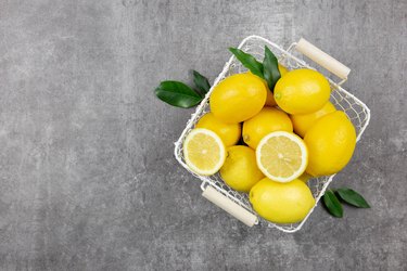 Fresh lemons with leaves in a basket on dark background. Vitamin C concept, immune defence.Top view. Copy space.