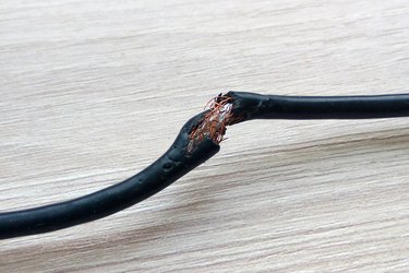 Damaged black electric cord on wooden table or floor background. Dangerous broken electrical cable