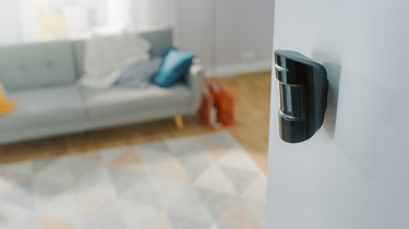 Close Up Object Shot of a Modern Movement Detector Unit on a White Wall in a Cozy Apartment in the Background.