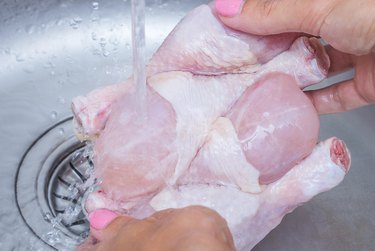 Woman washing raw frozen hen in kitchen sink. Cooking chicken at home. Close-up, selective focus.